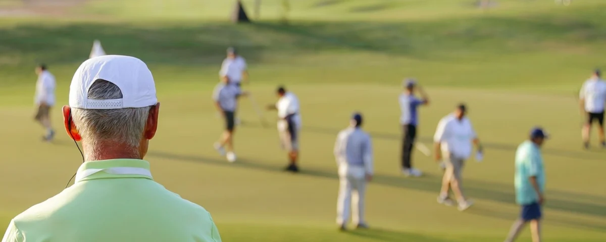 Sports event steward wearing an earpiece, supervising players on a golf green.
