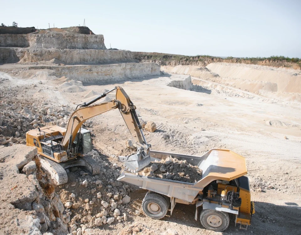 Excavator loading rock into a dump truck at a quarry, showing heavy plant and vehicle movements across the site.