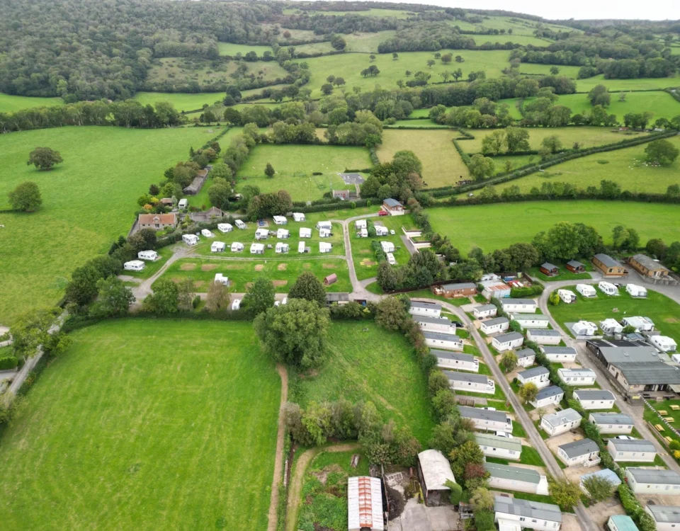 Aerial view of a holiday and caravan park with mobile homes, touring caravans, roads and surrounding countryside.